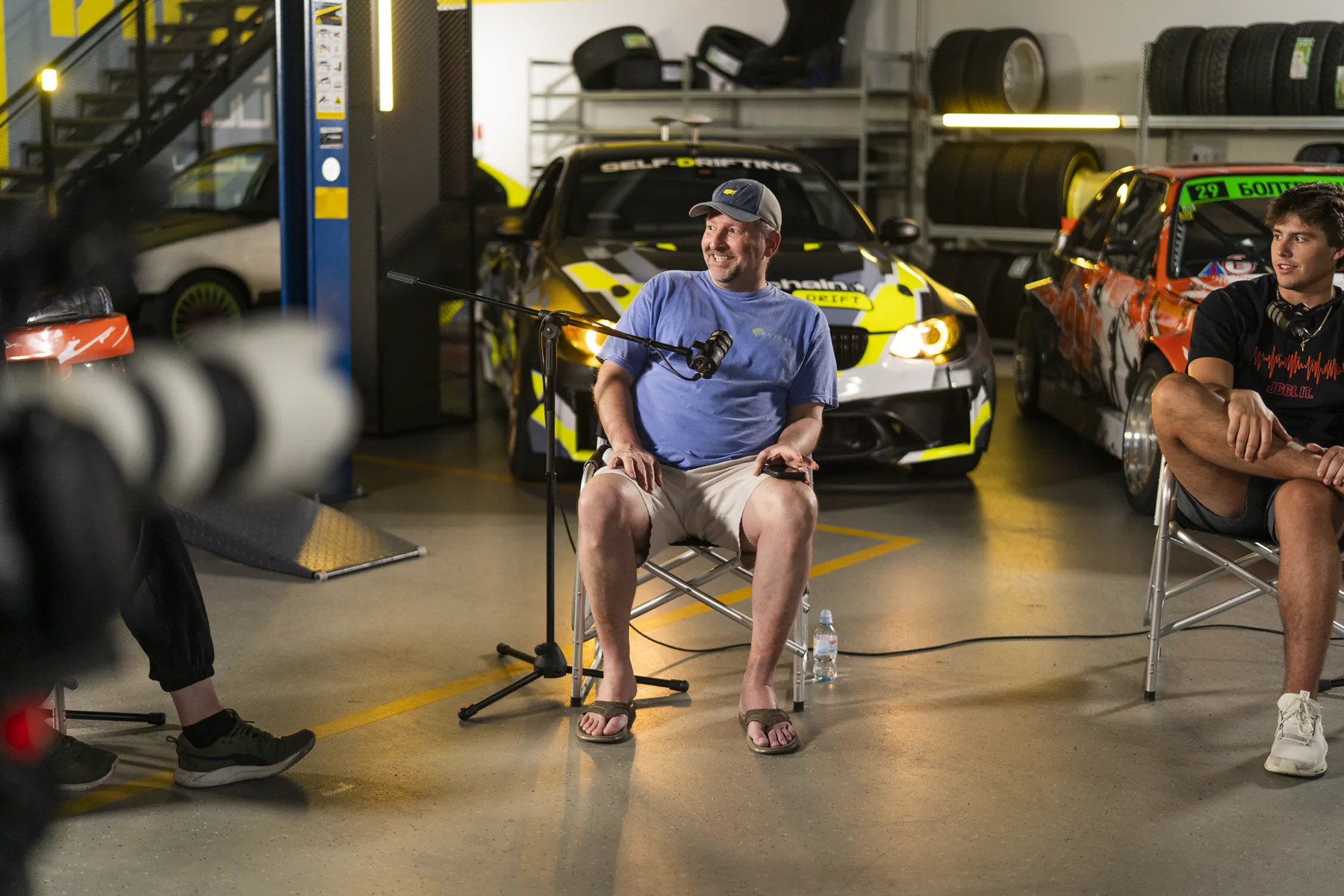 Brad Barton talking on camera in a garage with race cars