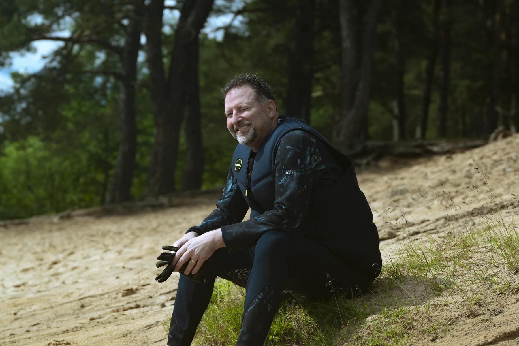 Brad Barton sitting on a sandy slope among pine trees, smiling