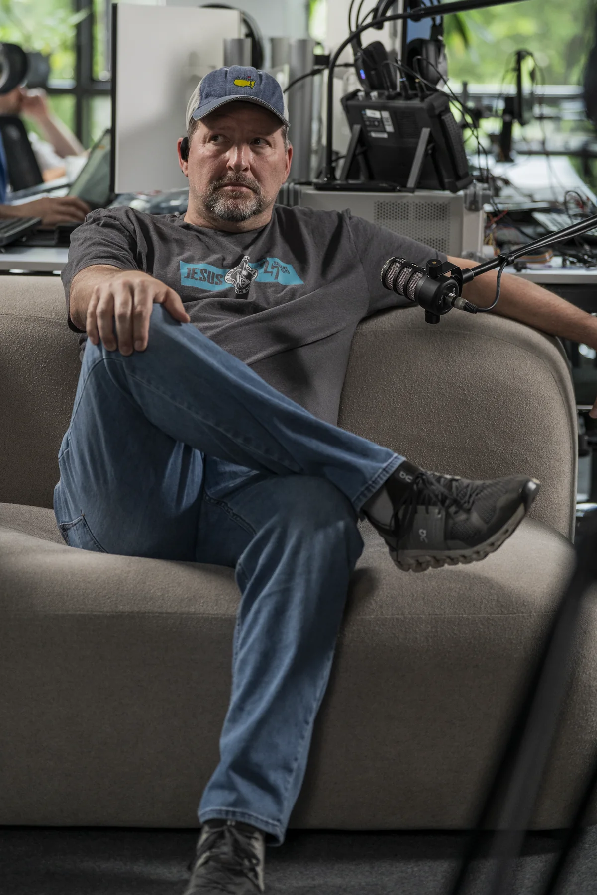 Brad Barton seated on a sofa in a studio, wearing a cap